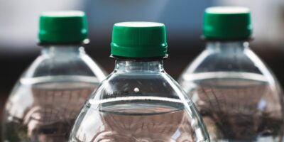 Focused view of three clear plastic bottles with green caps outdoors.